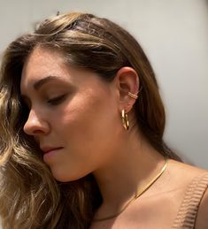 a woman with long hair wearing a gold necklace and matching earring is looking down at her left ear