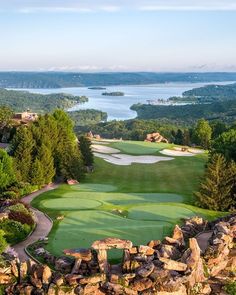 an aerial view of a golf course surrounded by trees and water with mountains in the background