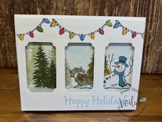 three christmas cards in a white box on a wooden surface with string lights and snowmen