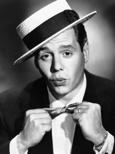 black and white photograph of a man wearing a hat with his hands on his tie