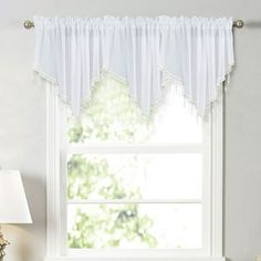 a window with a white curtain hanging from it's side next to a lamp