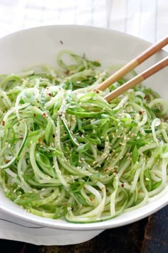 a white bowl filled with green noodles and chopsticks on top of a wooden table