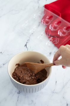 a person scooping chocolate into a bowl on a marble counter with red napkins