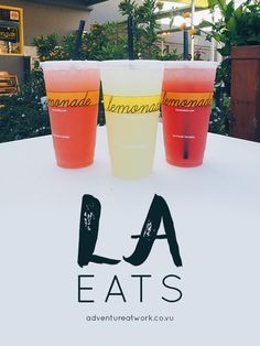 three drinks sitting on top of a table with the words la eats written in black