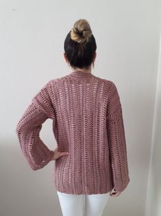 a woman standing in front of a white wall wearing a pink sweater and white pants