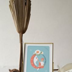 a cat sitting on a shelf next to a vase with flowers and a framed picture