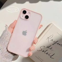 a person holding an iphone in their hand next to a book on a white table