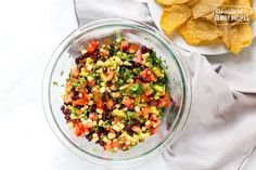 a glass bowl filled with corn and black bean salsa next to tortilla chips