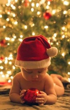 a baby wearing a santa hat on top of a bed next to a christmas tree