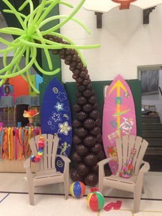 some chairs and surfboards in a room with balloons on the floor, palm tree and other decorations