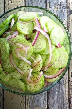 a glass bowl filled with sliced cucumbers and radishes on top of a wooden table