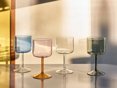 four wine glasses sitting on top of a table in front of a wall and window