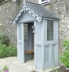 a small gray building sitting in the middle of a garden