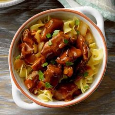 a bowl filled with meat and noodles on top of a wooden table next to a fork