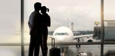 a man and woman standing in front of an airport window with their arms around each other