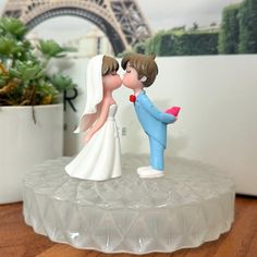 a wedding cake topper with a bride and groom kissing in front of the eiffel tower