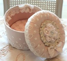 two round containers sitting on top of a table covered in white lace and fabric flowers