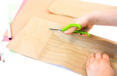 a person cutting paper with green scissors on top of some crafting material and colored pencils