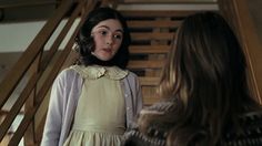 a woman standing in front of a staircase talking to another woman who is wearing a yellow dress