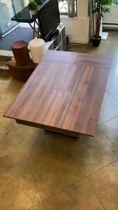 a wooden table sitting on top of a tile floor next to a tv monitor and potted plant