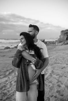 a man and woman standing on the beach with their arms around each other, hugging