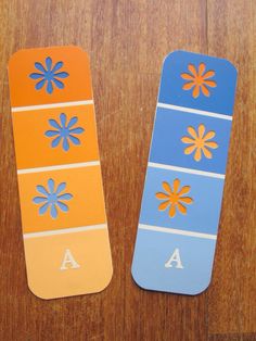 two skateboards with different designs on them sitting on a wooden surface, one painted orange and the other blue