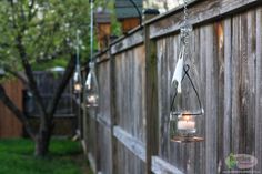 an outdoor candle holder hanging from a wooden fence in the backyard with lights on it