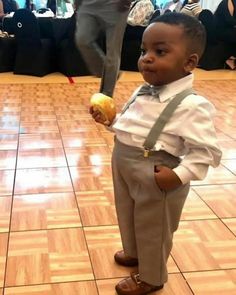 a young boy holding an apple in his right hand while standing on a wooden floor