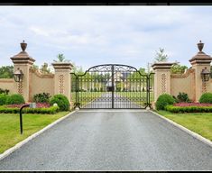 a gated driveway leading to a house with flowers in the foreground and bushes on either side