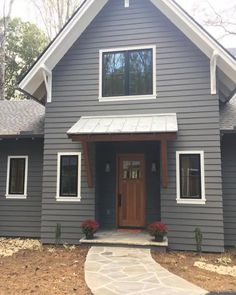 a gray house with white trim and wooden doors is shown in front of the entrance