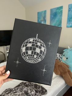 a person holding up a black box with a disco ball drawn on it in front of a bed