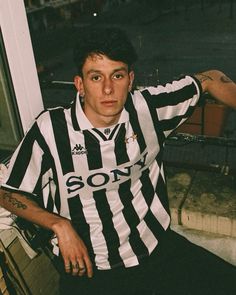 a young man sitting on top of a window sill wearing a black and white striped shirt