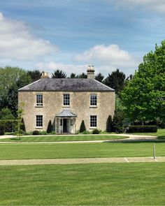 a large brick house sitting in the middle of a lush green field next to trees