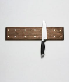 a knife is hanging on the wall next to a cutting board with holes in it