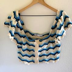 a blue and white crocheted top hanging on a wall next to a wooden hanger