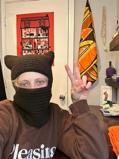 a woman wearing a knitted cat mask and making the peace sign with her hand