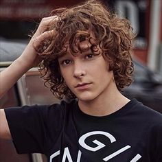 a young man with curly hair wearing a t - shirt that says gq on it