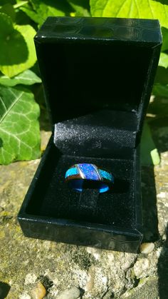 a blue ring in a black box sitting on top of a stone surface next to green leaves