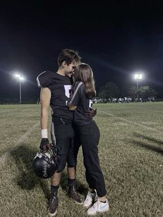 two people standing in the middle of a field at night with their arms around each other