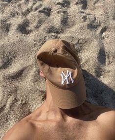 a man laying in the sand wearing a new york yankees baseball cap with white letters on it