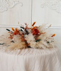 an arrangement of dried flowers and feathers on a white table cloth in front of a mirror