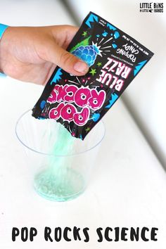 a hand holding a pop rocks science kit over a cup filled with green liquid and sprinkles