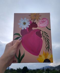 a person holding up a painting with flowers on it in front of a cloudy sky