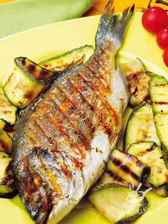 grilled fish with zucchini and tomatoes on a yellow plate, ready to be eaten