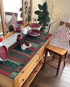 a wooden table topped with plates and bowls next to a mirror on top of a hard wood floor