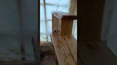 a wooden bench sitting next to a window in a room with unfinished walls and wood flooring