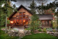 a log cabin is lit up at night with lights on the porch and steps leading to the front door