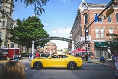 a yellow car is driving down the street in front of some tall buildings and people