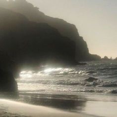 the sun shines through the foggy mist on an ocean beach with waves coming in