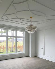 an empty room with a chandelier hanging from the ceiling and large windows on both sides